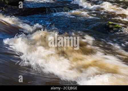 Running water in chaos with the sun illuminating the water among rocks in Vattenfallet which is located in Älvkarleby Sweden Stock Photo
