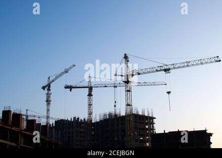 Hydraulic luffing jib tower cranes and workers being poured concrete into foundation. Cement pouring into formwork of building at construction site. T Stock Photo