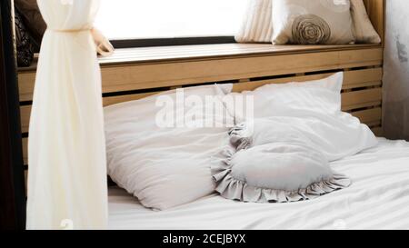 Bed in the bedroom at the window with textured coverlets with plaids and pillows Stock Photo