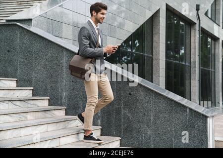 Image of cheerful handsome business man outdoors using mobile phone while going down the stairs Stock Photo