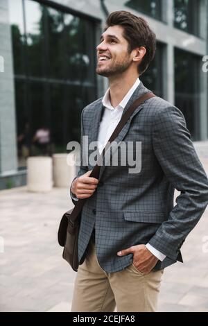 Image of cheerful smiling handsome business man outdoors near business center Stock Photo