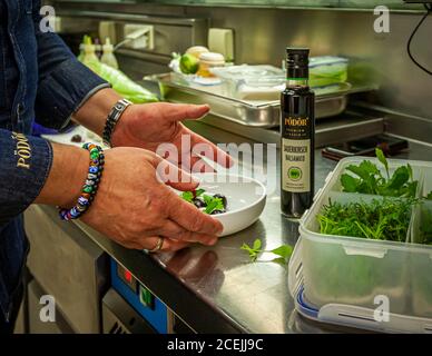 A cook arranges dark berries and herbs by hand into a small dish, next to it a bottle of PÖDÖR sour cherry balsamic and a crate of fresh herbs, in the kitchen of Thomas Bühner's restaurant "la vie" in Osnabrück, Germany – the three-Michelin-star restaurant closed only weeks after this photograph, in July 2018. Stock Photo
