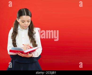 schoolgirl writing notes on orange background. reading lesson. get information form book. back to school. little child concentrated on work. small girl in school uniform. writing in workbook. Stock Photo