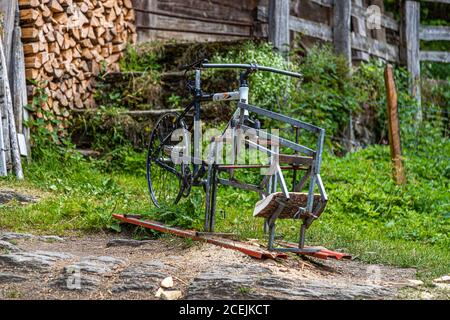 A wood-sawing device built from a discarded bicycle cuts firewood using pure muscle power in Lenk, Switzerland. A log already rests on the red sled, with freshly cut firewood stacked in the background. Stock Photo