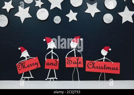 Stick man family figure wearing santa hat holding a red Merry and Safe Christmas greeting banner. Covid holidays celebration concept. Stock Photo
