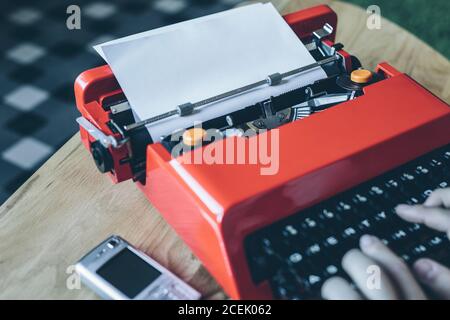 Mobile phone near crop close-up hands typing on bright red typewriter Stock Photo