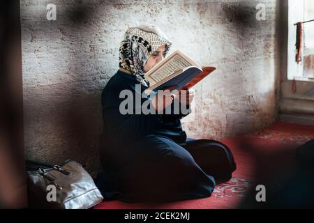 Istanbul, Turkey - August, 17 2018: Islamic woman in traditional clothes sitting and reading book Stock Photo