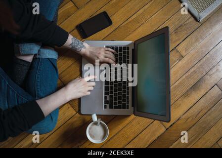 Crop Woman typing on laptop on floor Stock Photo