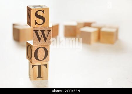 Four wooden cubes arranged in stack with text SWOT (meaning Strengths, Weaknesses, Opportunities and Threats) on them, space for text / image at down Stock Photo