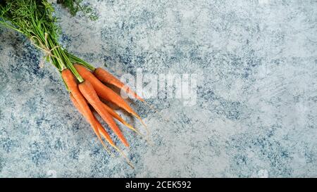 Bunch of carrots with green leaves on blue marble like board, view from above Stock Photo