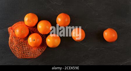 Top down view - oranges in net, some scattered on black stone like board Stock Photo