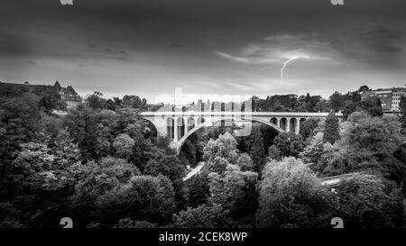 Black and White Photo of the Pont Adolphe (Adolphe Bridge) and Vallé de la Pétrusse (Petrusse Park), with  a Lightning Strike in the distance Stock Photo