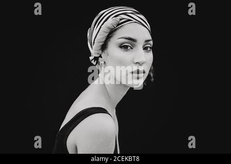 Side view of beautiful young Woman in striped head cloth with bright makeup looking at camera isolated on black background Stock Photo