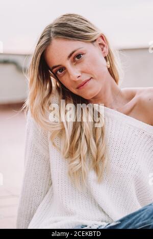Young pretty Woman with fair hair in white pullover sitting outside at daylight and looking at camera Stock Photo