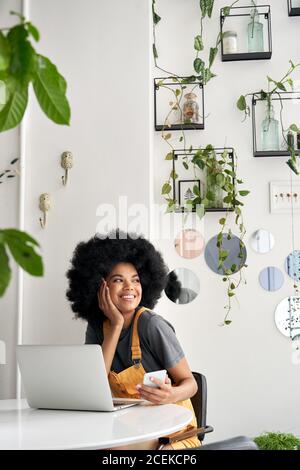 Happy African hipster lady looking through window sitting at table in cozy cafe. Stock Photo