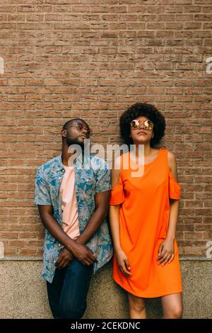 Attractive African-American man and Woman in stylish outfits standing near brick wall on street Stock Photo