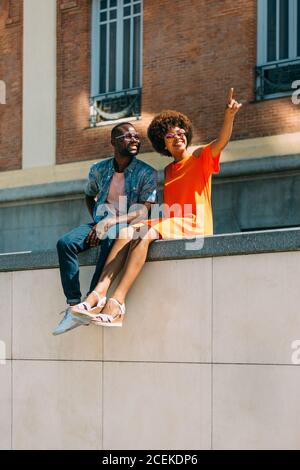 smiling black couple sitting on border and pointing Stock Photo