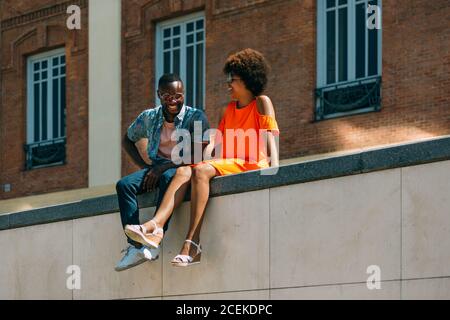 Attractive African-American man and Woman laughing and leaning on each other while sitting on border on city street Stock Photo