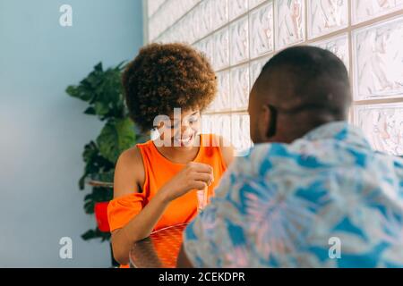 Side view of black man and Woman smiling and looking at each other while sitting at cafe table and having drink Stock Photo
