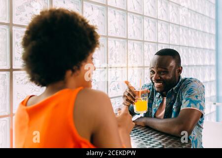 Side view of black man and Woman smiling and looking at each other while sitting at cafe table and having drink Stock Photo