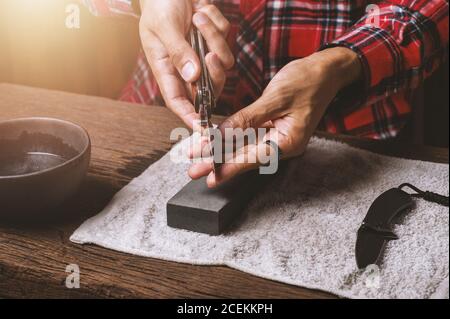 The man using whetstone to sharpening his pocket knife. Pocket knife care and maintenance concept. Stock Photo