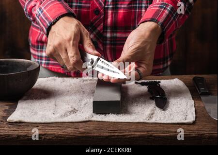 Man Sharpening His Pocket Knife with a Whetstone on a Rustic