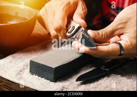 Man sharpening his pocket knife with a whetstone on a rustic wooden table  Stock Photo - Alamy