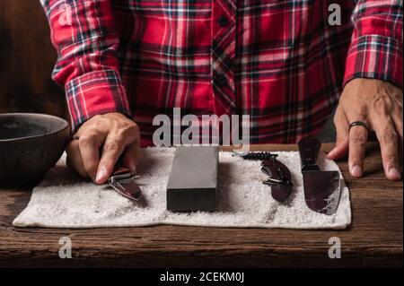 Man sharpening his pocket knife with a whetstone on a rustic wooden table  Stock Photo - Alamy