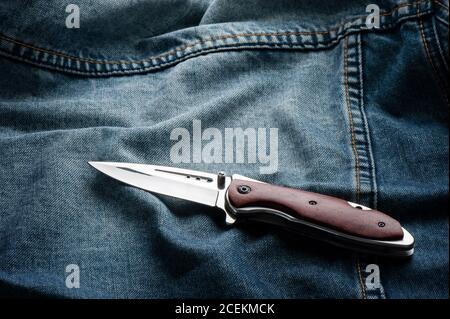 stainless steel folding knife with wooden handle isolated on Jeans. Stock Photo