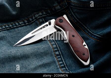 stainless steel folding knife with wooden handle isolated on Jeans. Stock Photo