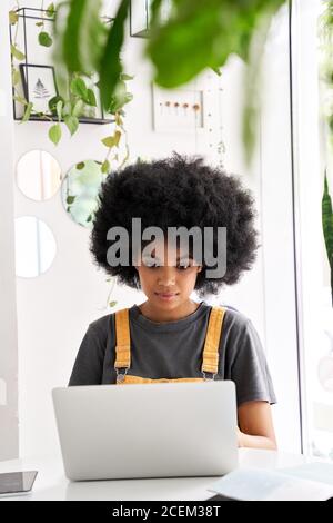 Happy African lady student using laptop sitting at table at home, in cafe. Stock Photo