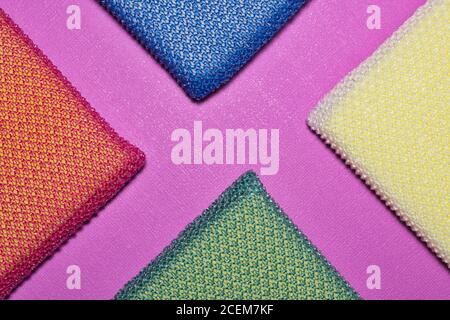 Colorful cleaning sponges arranged in triangle diagonals on a peony colored background. Vibrant full frame image. Stock Photo