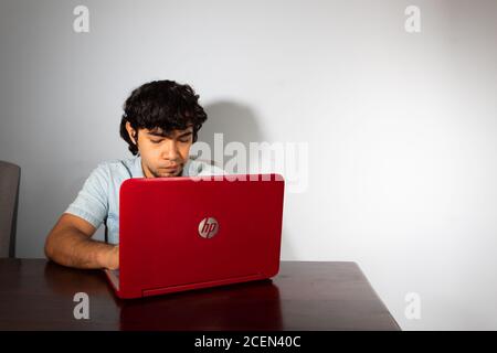 Young hispanic wavy hair man studying from home with a laptop, looking pensive Stock Photo