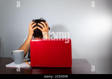 Wavy-haired young hispanic man studying from home with a laptop. tired and frustrated from studying or working Stock Photo