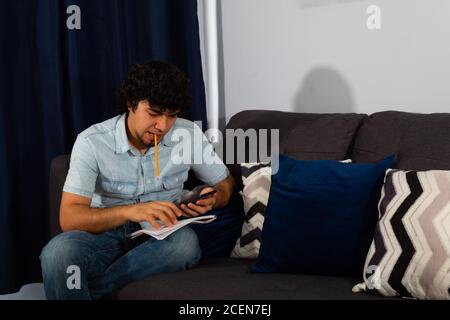 Young hispanic man with wavy hair studying from home with a cellphone Stock Photo