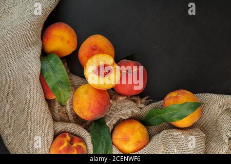 Peaches on a black background with burlap fabric and green leaves. Sweet and juicy peach slices with a stone Stock Photo