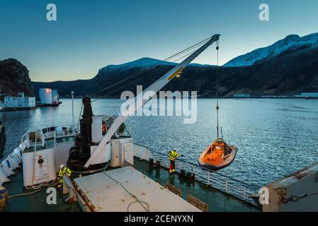 Unloading cargo with crane from freighter in the port of the city Maloy in Norway seen from cruise ship in early morning Stock Photo
