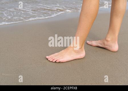 Close-up of child's legs walking on sand coast and sea water. Young girl legs on baltic sea beach. Teenager legs near sea line.
