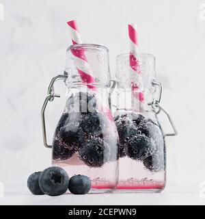 Joy bright fresh summer drinks with blueberry, straw, soda water in elegant yoke bottles on soft light white wood table, square. Stock Photo