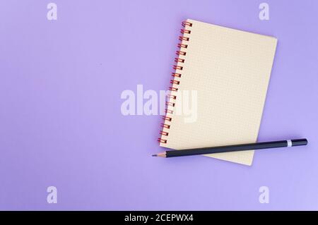 Closeup of a notebook and a pencil isolated on a purple background Stock Photo