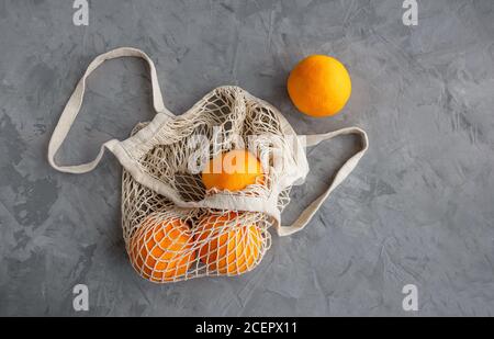Ripe oranges in a white string bag. Gray concrete background. Copy space. Flat lay. Stock Photo