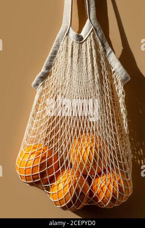 Ripe oranges in a white string bag. Beige background. Close-up. Stock Photo