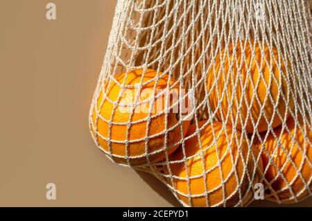 Ripe oranges in a white string bag. Beige background. Close-up. Copy space. Stock Photo