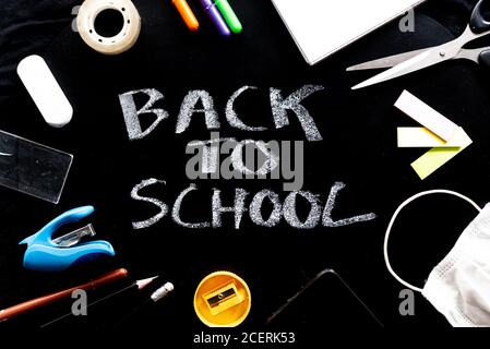 back to school text on blackboard, concept of college education in the time of covid19 pandemic, with face mask and stationery Stock Photo