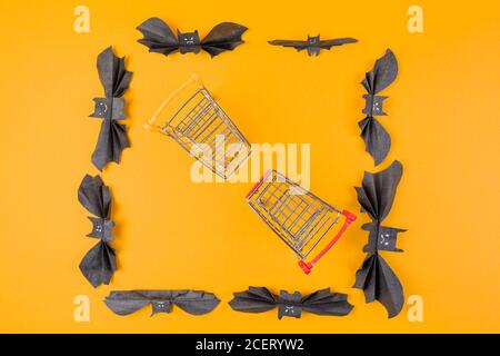 Two shopping toy carts are located in a frame of paper decorative bats. Orange background. Copy space. Flat lay. The concept of Halloween and holiday Stock Photo