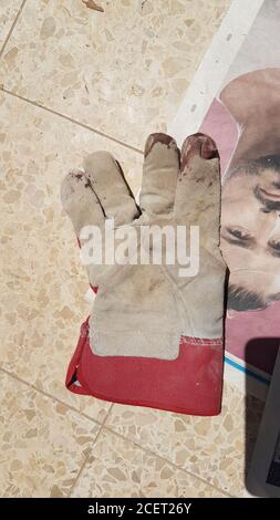 Blood stained gloves while using an electric rotary saw the worker injured his thumb on the revolving blade. luckily, the operator was wearing protect Stock Photo