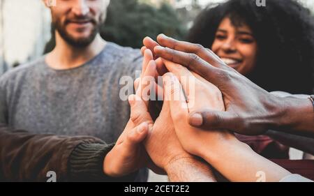 Young happy people stacking hands outdoor - Diverse culture students celebrating together - Focus on hands Stock Photo