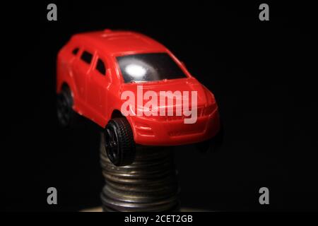 Saving money for a car. Banking, fast. Toy car and coins on black background. Miniature red car model on growing stack of coins. Finance and car loan. Stock Photo