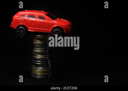 Saving money for a car. Banking, fast. Toy car and coins on black background. Miniature red car model on growing stack of coins. Finance and car loan. Stock Photo
