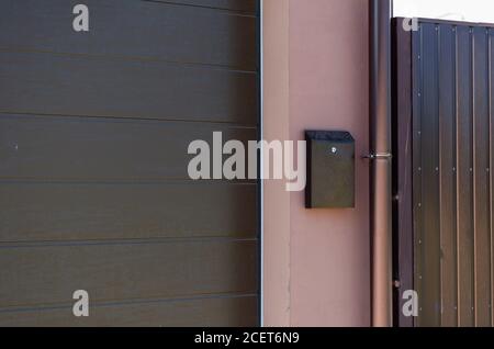 A brown letterbox on the pink wall next to the downpipe. The garage doors are closed with protective shutters on the left. Real estate and architectur Stock Photo